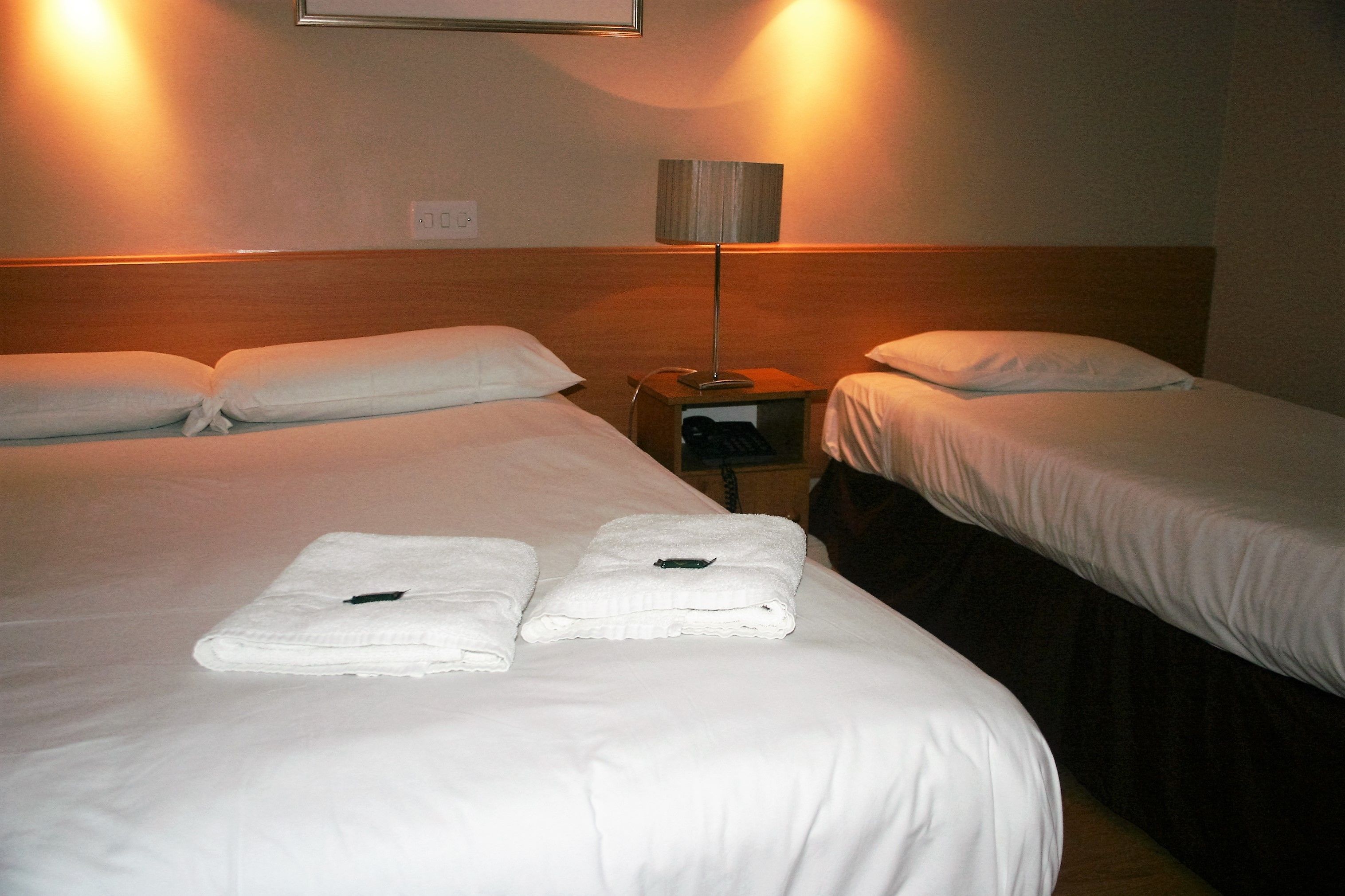A hotel room with two beds, a nightstand, and a lamp.