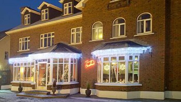 A multi-story brick building with large windows and a neon sign. - St Judes Lodge (Galway)
