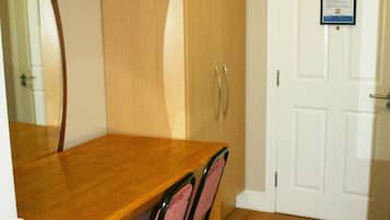 Une table à manger en bois avec des chaises, une porte blanche avec un avis affiché, et un miroir au mur.