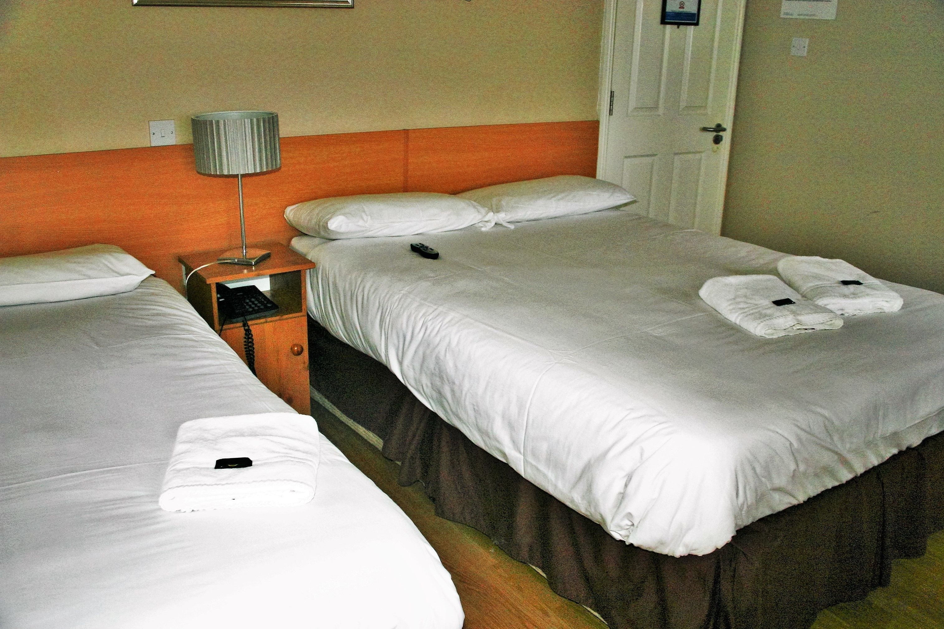 A hotel room with two beds, a nightstand, a lamp, and a door.