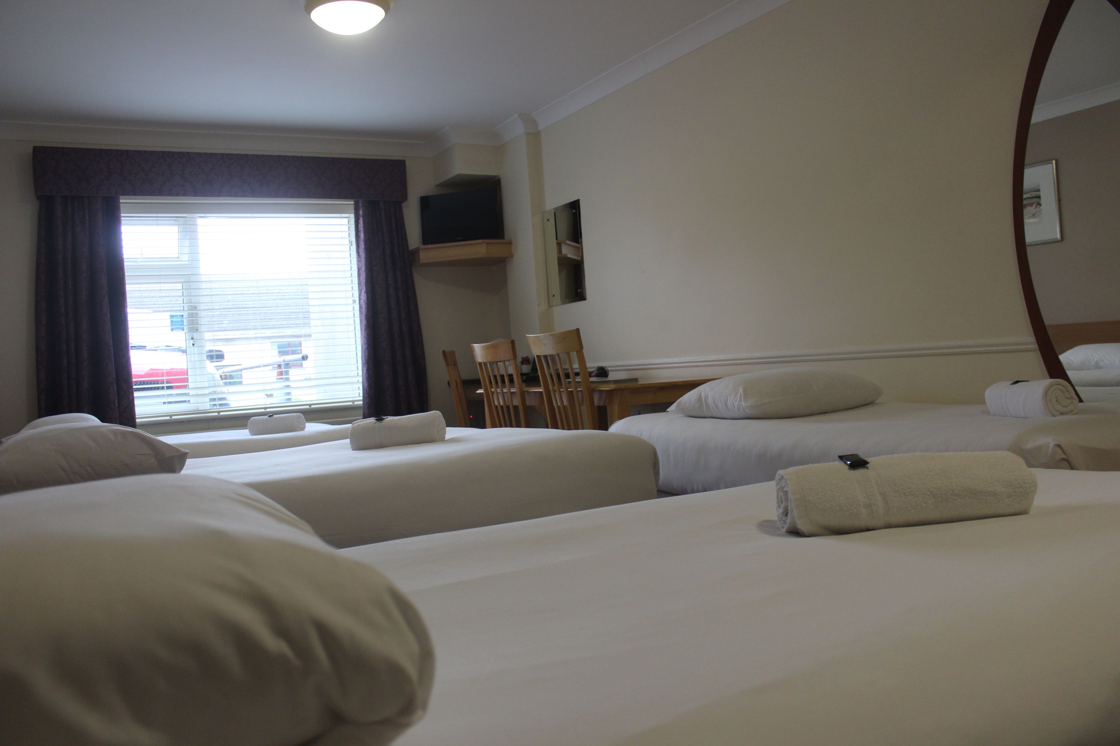 Une chambre d’hôtel avec deux lits, un bureau, une chaise et une grande fenêtre avec des rideaux.