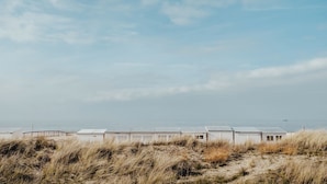 Una hilera de cabañas blancas en la playa, con arena al frente y un mar tranquilo de fondo.