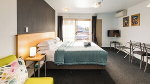Ein Hotelzimmer mit Bett, Schreibtisch, Stuhl, Fernseher und einem Fenster mit Vorhängen.