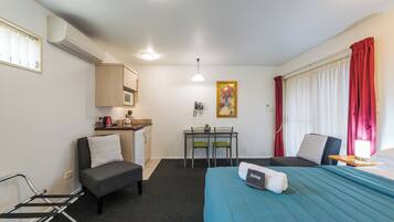 Une chambre d’hôtel de taille réduite, comprenant un lit, un bureau avec une chaise, une kitchenette et une fenêtre avec des rideaux.