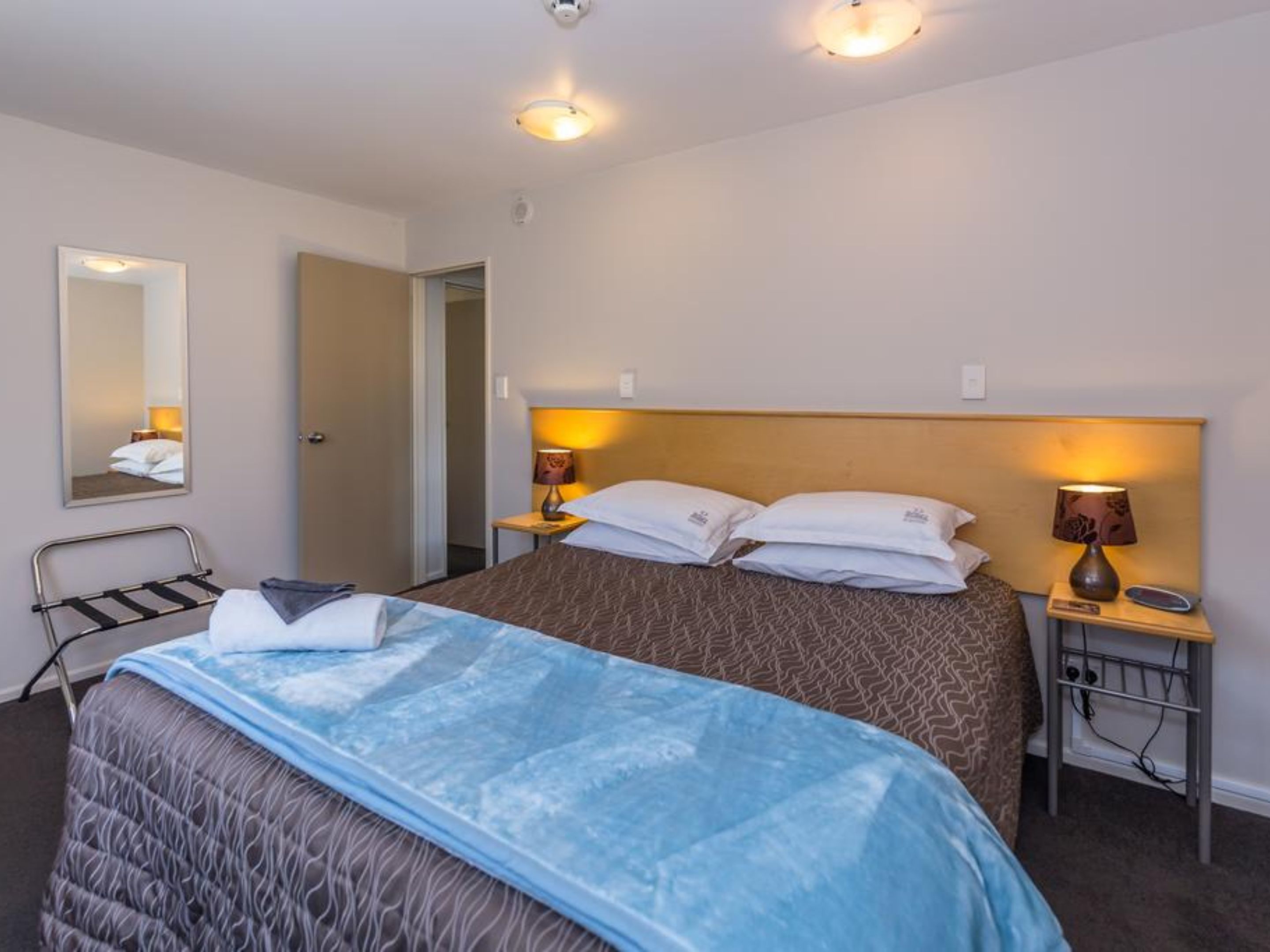 Et hotelværelse med en seng, sengeborde med lamper, et spejl og en dør.