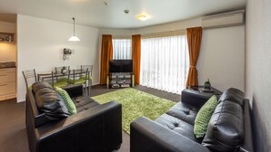 Ein modernes Wohnzimmer mit Fernseher, Ledersofas, einem Esstisch und einem grünen Teppich.