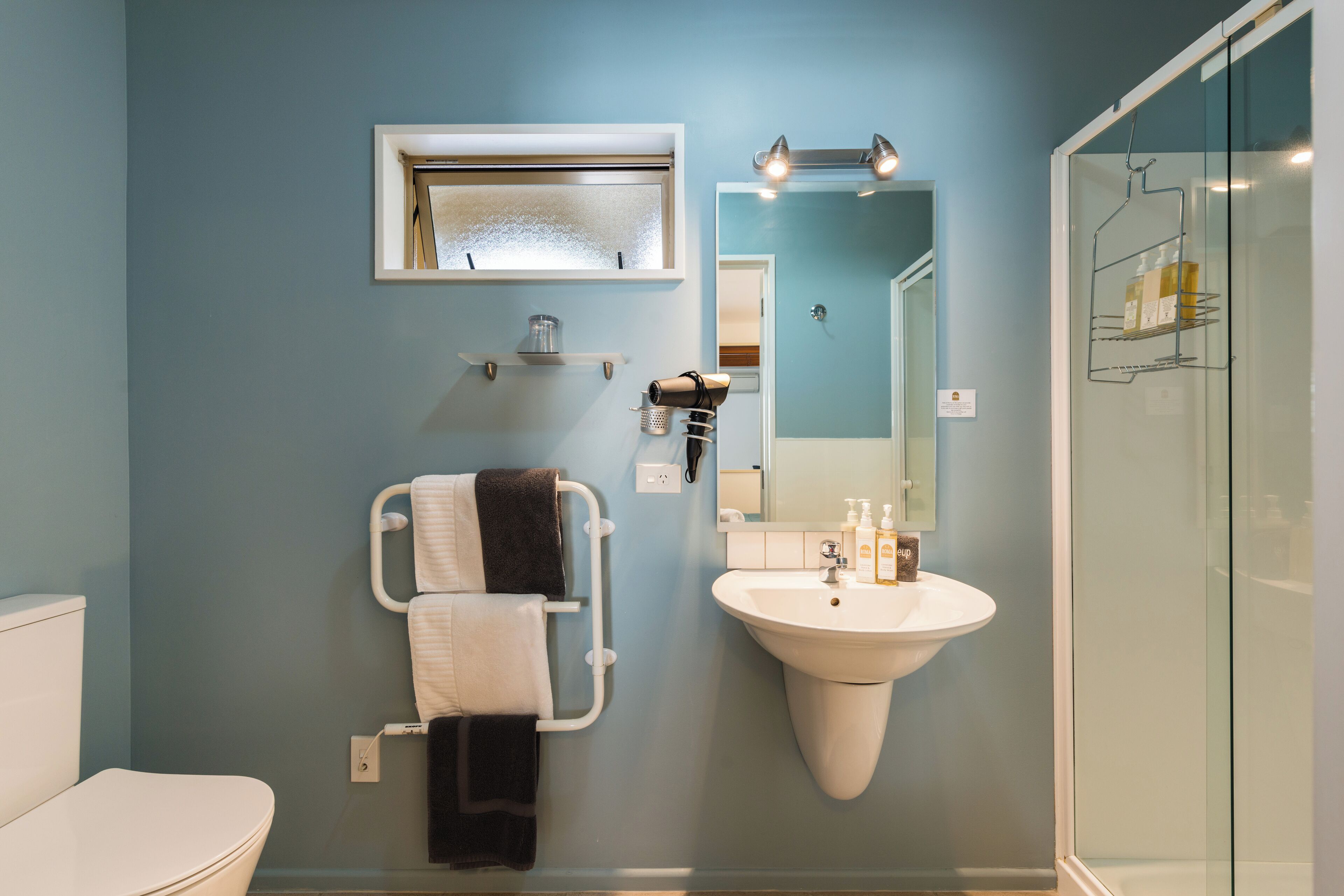 A bathroom with a white sink, a towel rack with towels, a mirror, and a shower area.