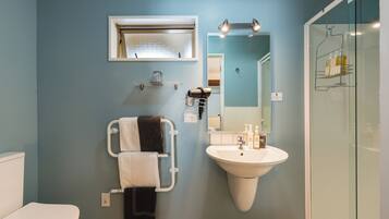 Une salle de bain avec un lavabo blanc, un porte-serviettes avec des serviettes, un miroir et un espace douche.