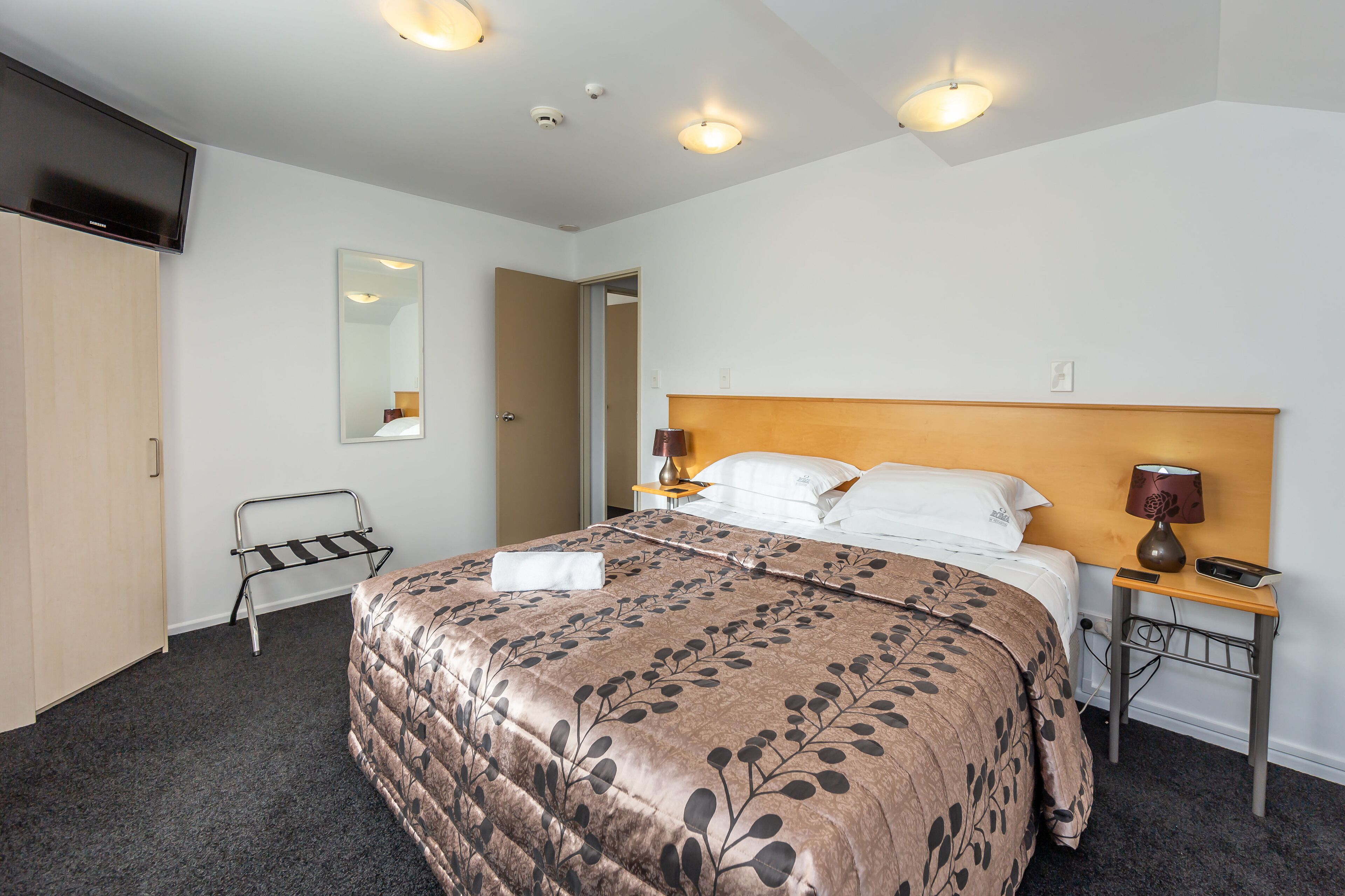 Habitación de hotel con una cama grande, una mesita de noche con lámpara, un espejo y un armario.