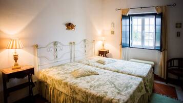 Quarto com duas camas, uma janela com cortinas e duas luminárias de cabeceira.