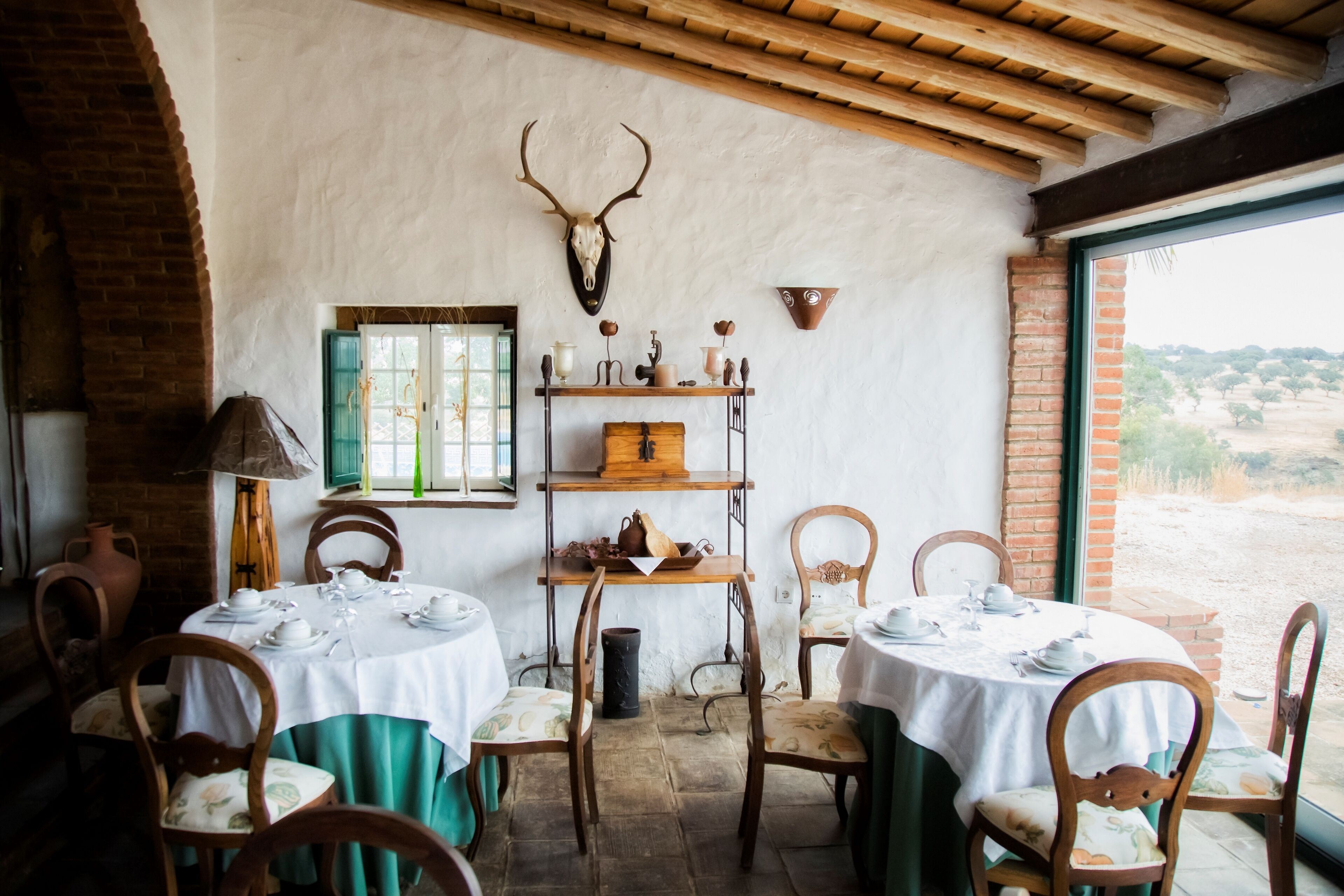 Un comedor rústico con mesas y sillas de madera, pared de ladrillo y un cráneo de venado montado.