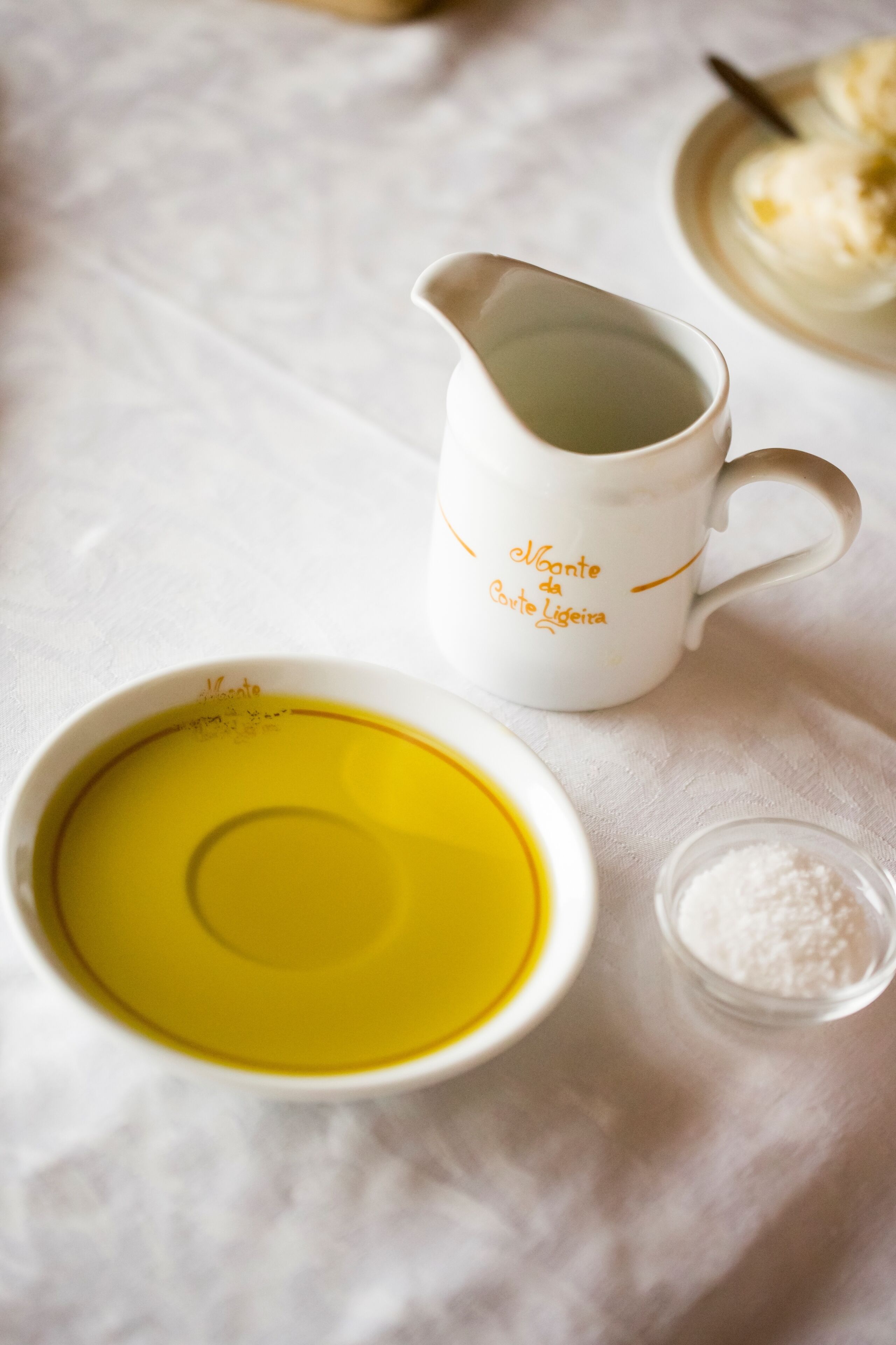 Una mesa blanca con una jarra blanca, un recipiente con líquido amarillo y un pequeño envase de polvo blanco.