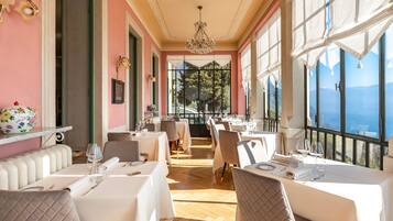 A restaurant with white tables and chairs, a chandelier, and large windows offering a view of the mountains.