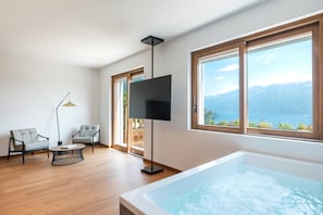 Un salón moderno con un gran ventanal, un televisor de pantalla plana, dos sofás grises, una mesa de centro y una bañera.