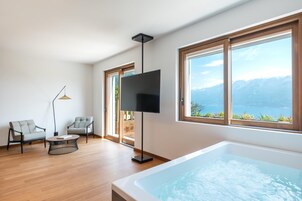 Un salón moderno con un gran ventanal, un televisor de pantalla plana, dos sofás grises, una mesa de centro y una bañera.