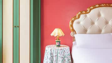 Una stanza con un letto, un armadio verde e bianco e un tavolo con una tovaglia floreale e una lampada.