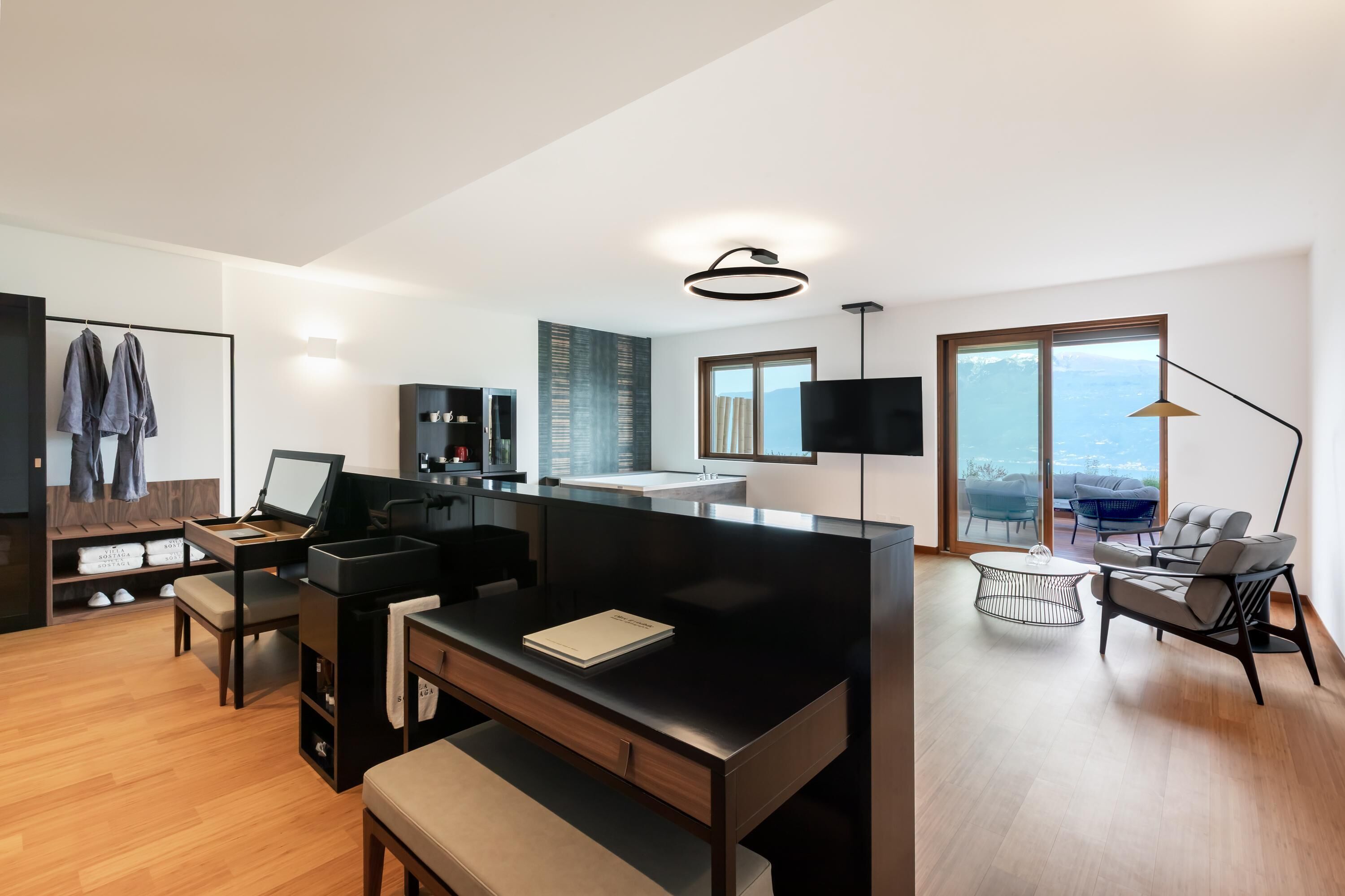 Una sala de estar moderna con un sofá negro, una mesa de comedor y una zona de cocina con un ventanal grande.