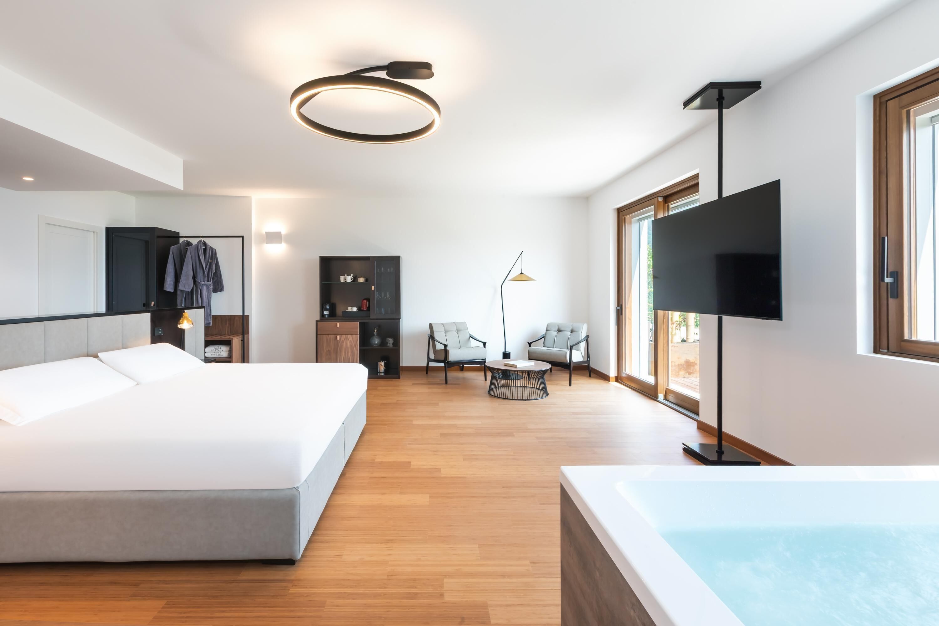 A modern hotel room with a large bed, a TV, a seating area with chairs, a small table, and a bathtub.
