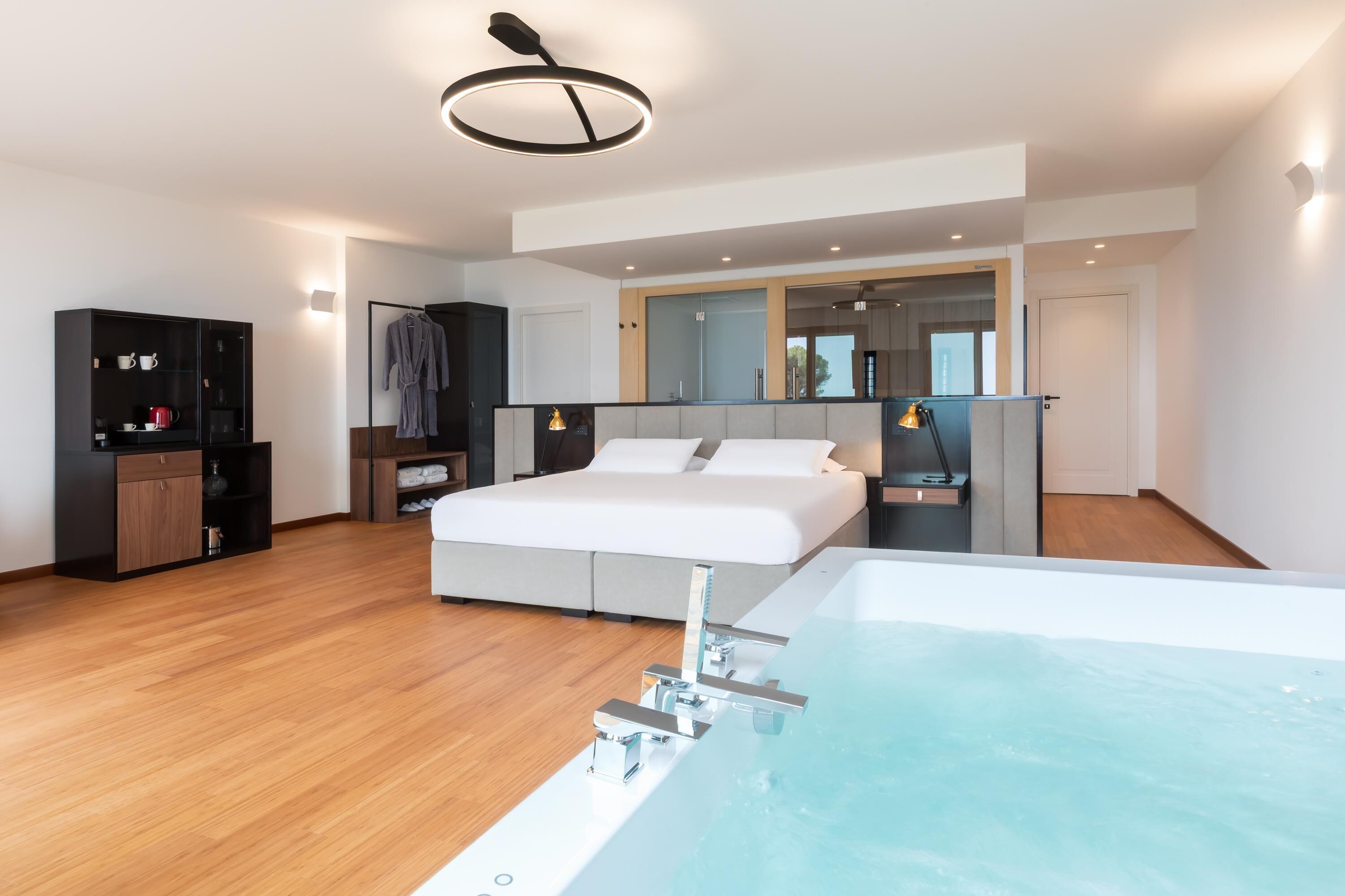 Una habitación de hotel moderna con una cama grande, una bañera integrada, un armario y un espejo sobre la cama.