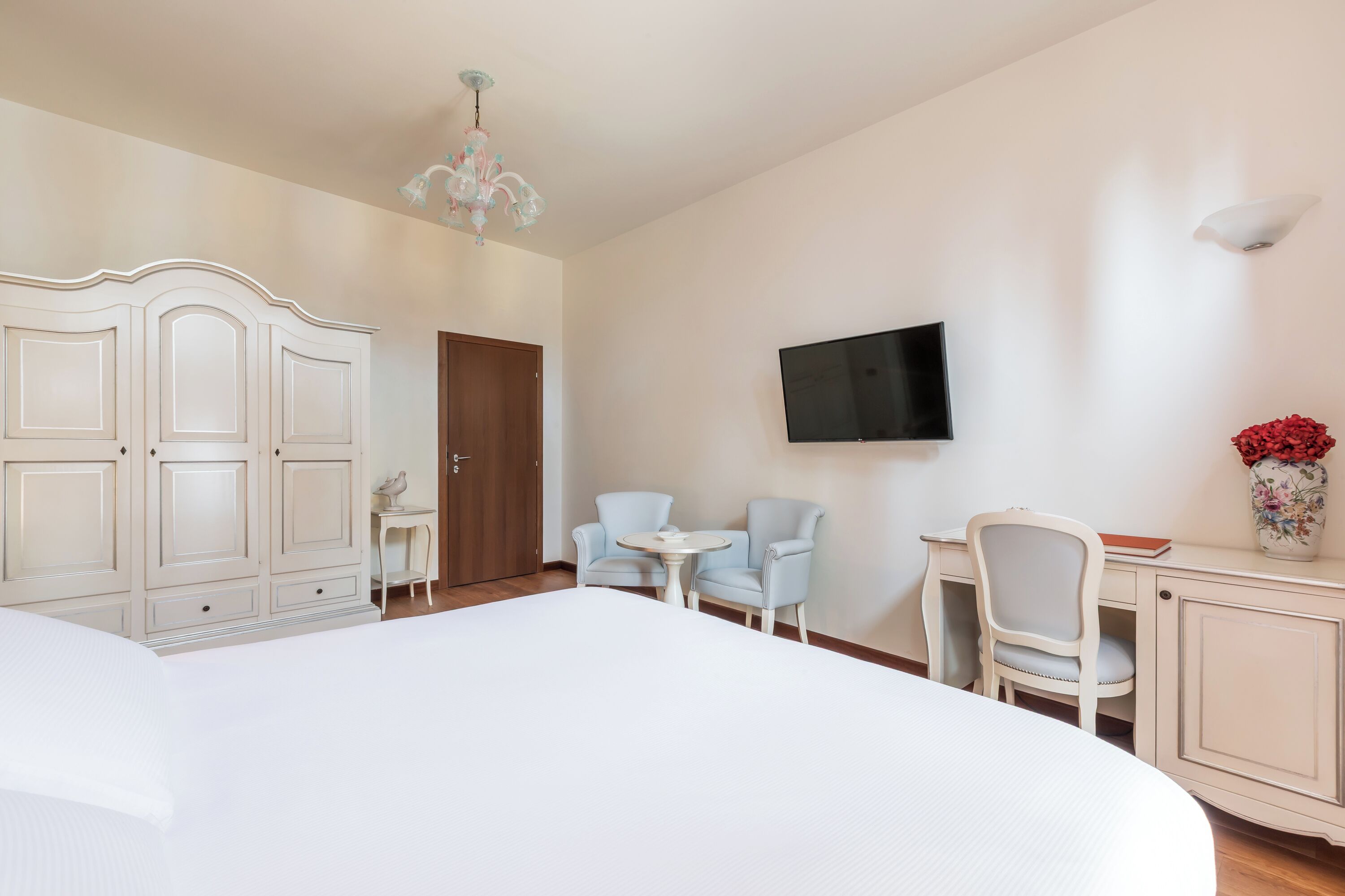 A hotel room with a large bed, a desk with two chairs, a television mounted on the wall, and a door.