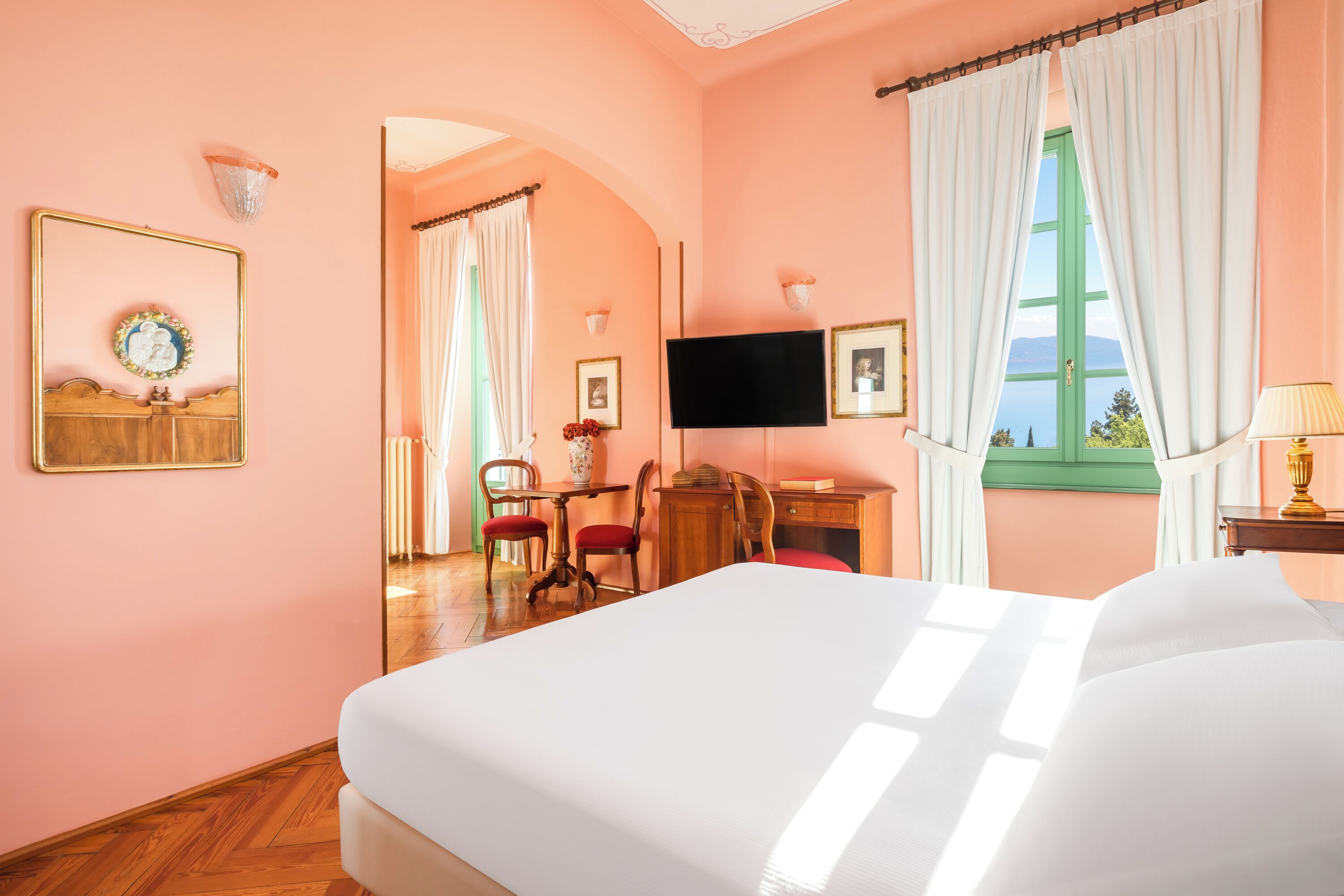 Une chambre d’hôtel avec un grand lit, un bureau avec une chaise, une télévision et une fenêtre avec des rideaux.