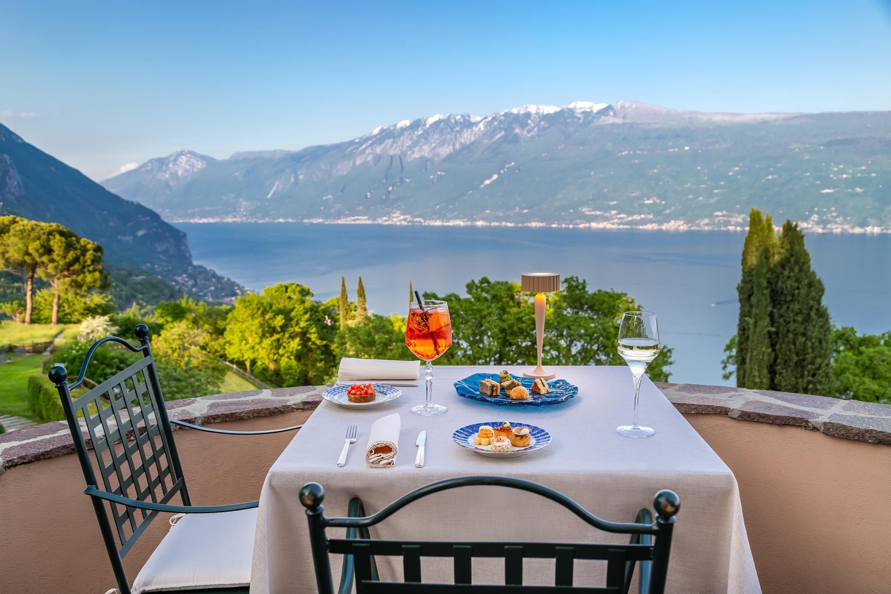 Una mesa servida con platos de comida, copas de vino y una vista panorámica de un lago y montañas.