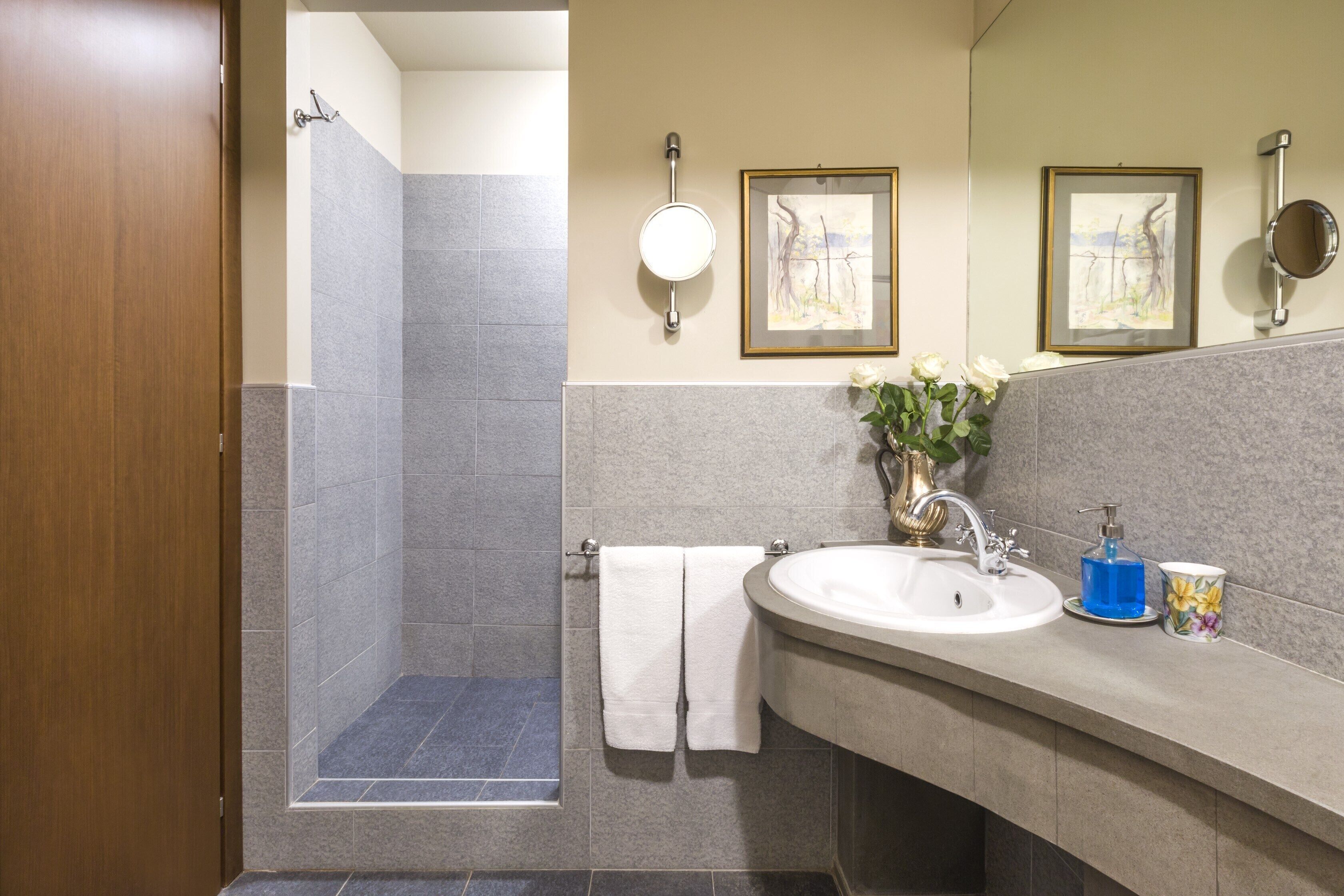 Un bagno con doccia, lavandino e due quadri appesi al muro.