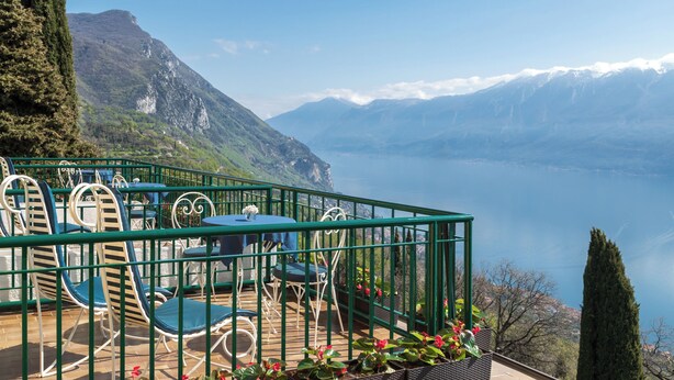 A terrace with outdoor seating, overlooking a lake and mountains.