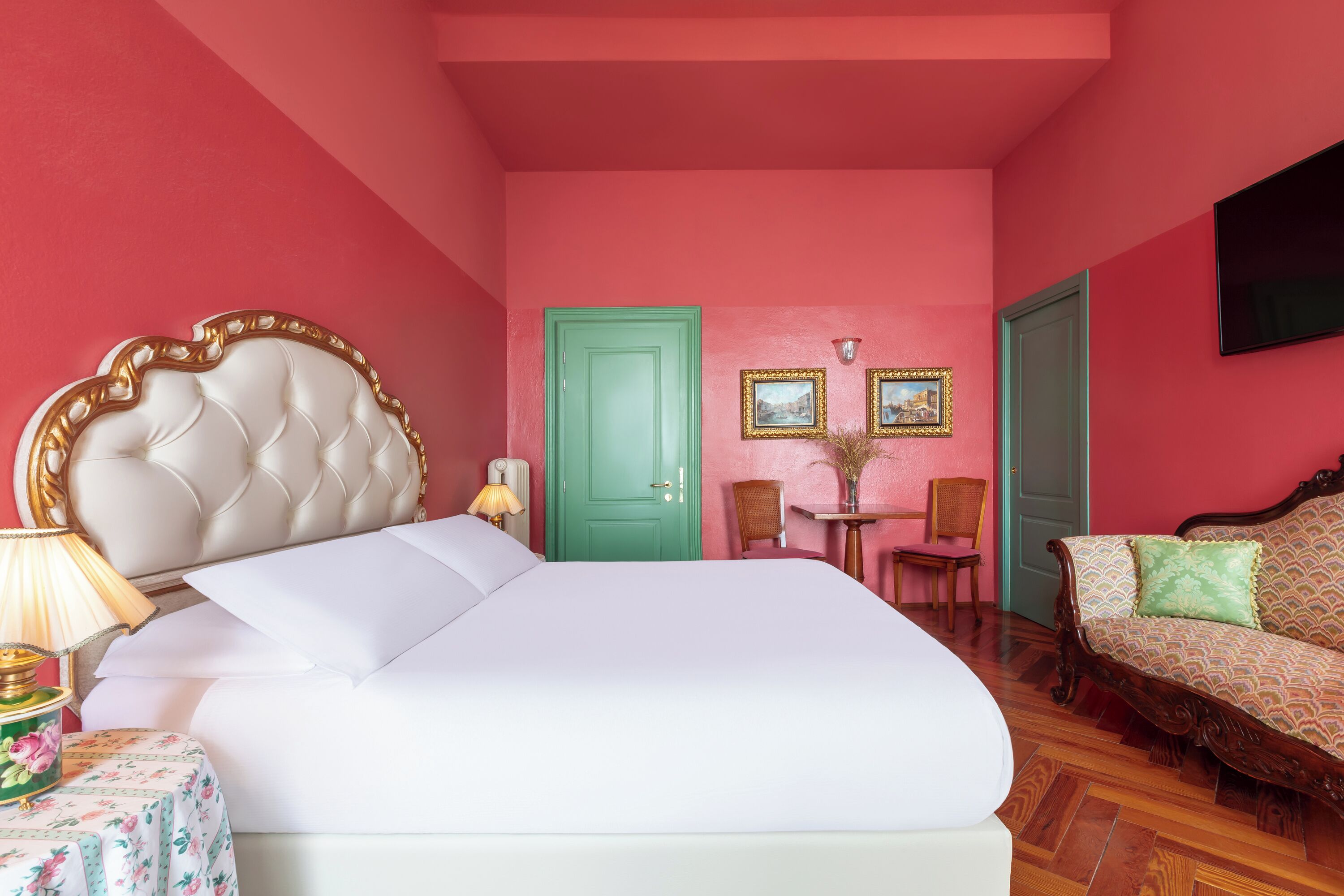A bedroom with a large bed, a green door, two framed pictures, a small table with chairs, and a sofa.