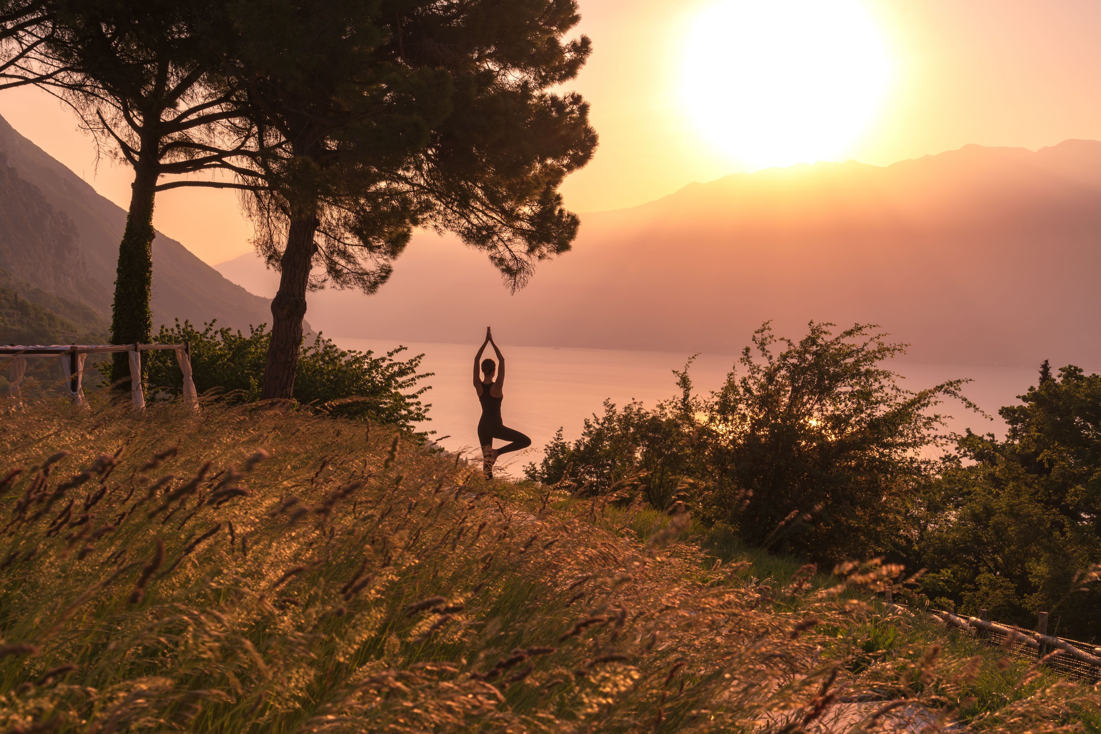 A person practicing yoga on a grassy hill with a mountain backdrop and a body of water.
