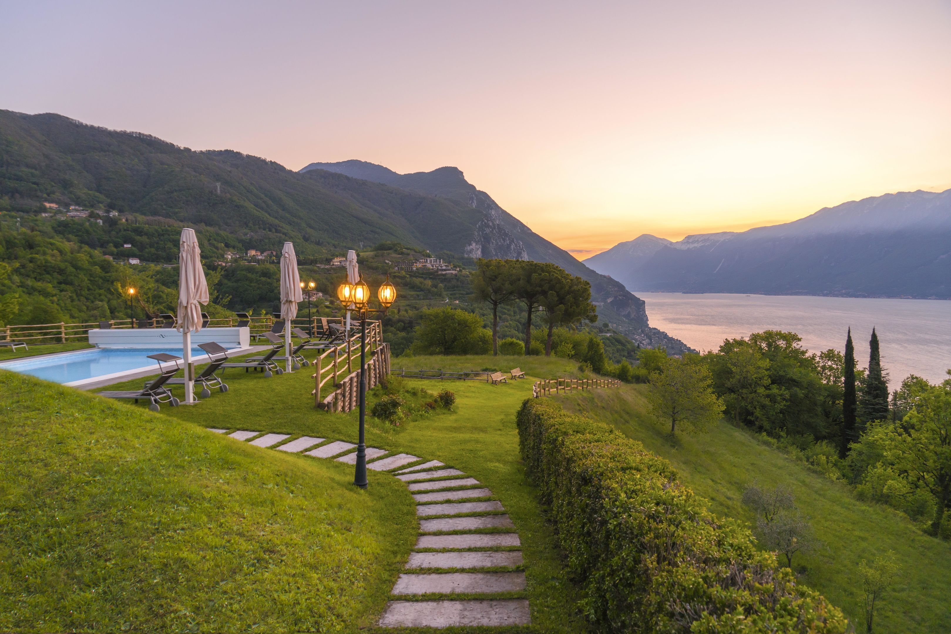 A pool area with lounge chairs, a staircase, and a view of the lake and mountains.