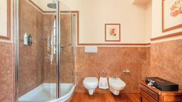 Ein Badezimmer mit Duschkabine, Toilette, Bidet und einem hölzernen Waschtisch mit einer Schachtel darauf.
