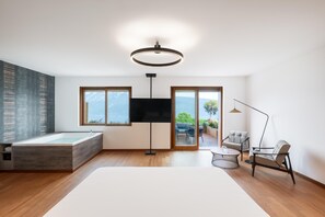 A modern living room with a large window, a flat-screen TV, a floor lamp, and a sofa. - Boutique Hotel Villa Sostaga (Gargnano)