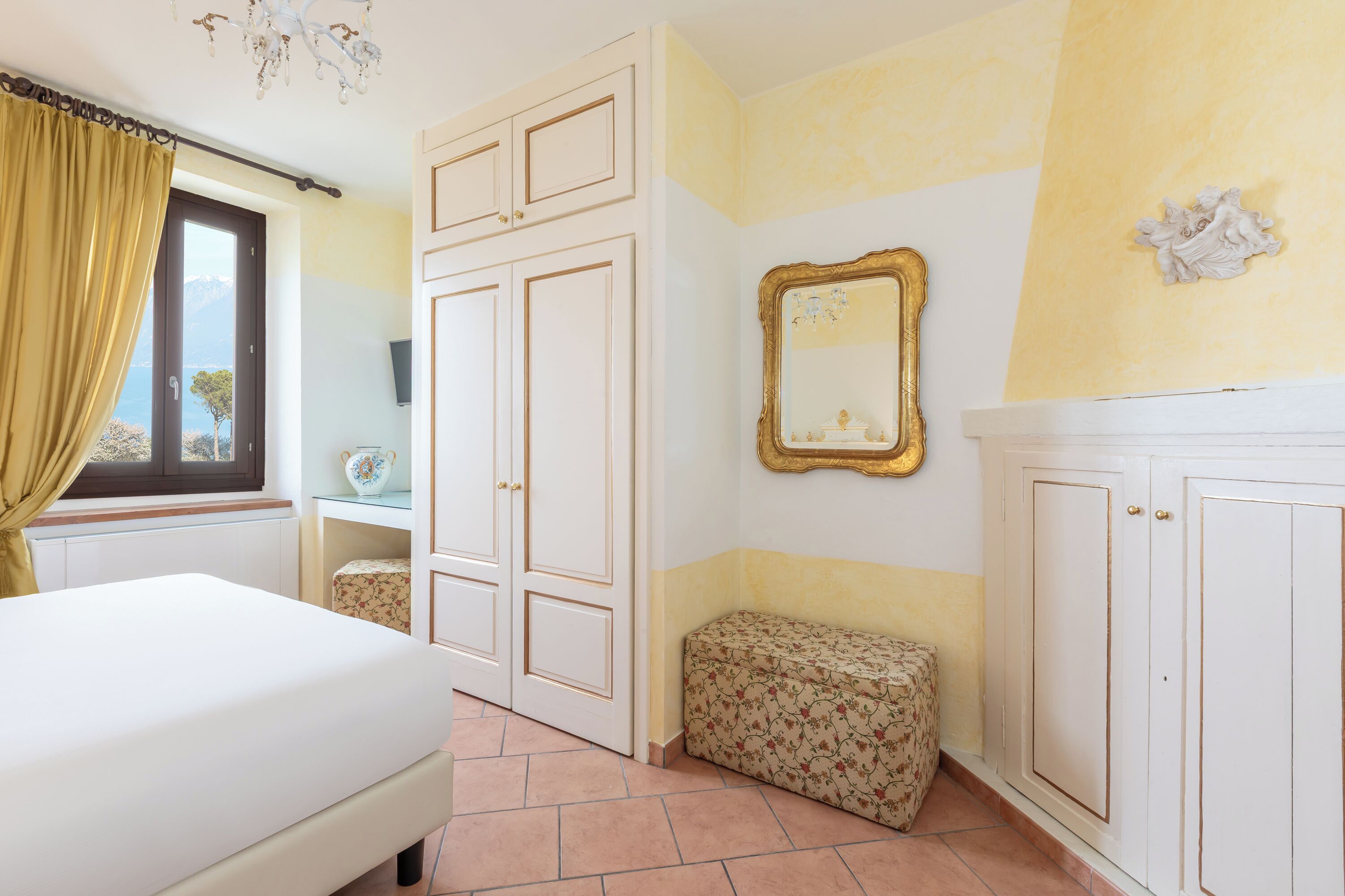 Quarto com cama, cómoda, um banco e janela com vista.