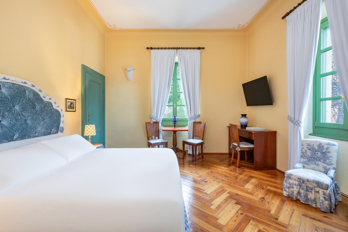 Habitación de hotel con cama, escritorio con sillas, televisión y ventana con cortinas.