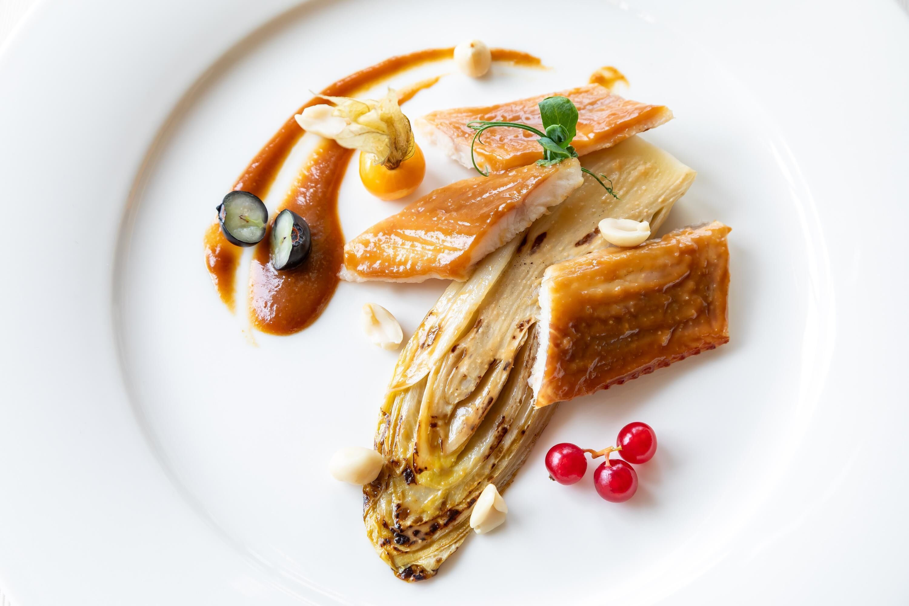 A white plate with a dish of grilled artichoke, salmon, and garnishes.