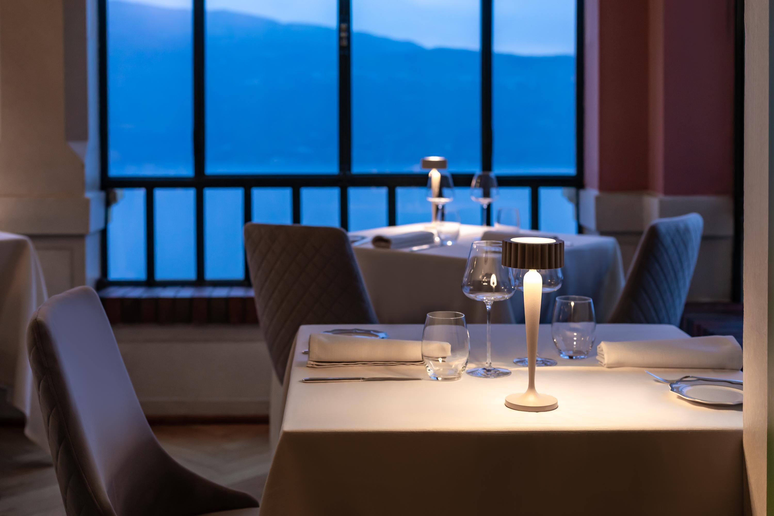 A dining table set for two with a view of the sea through large windows.