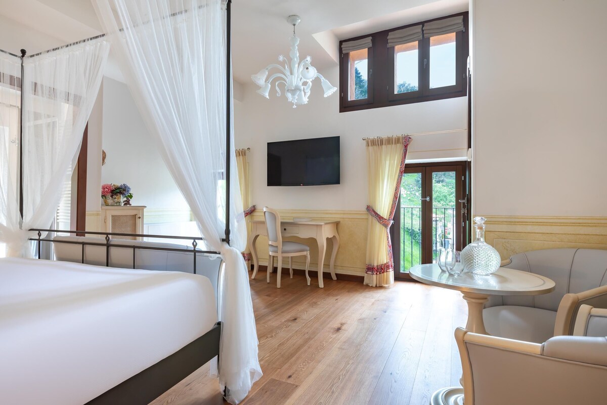 Un dormitorio con cama, escritorio, silla, televisor y vistas al exterior.