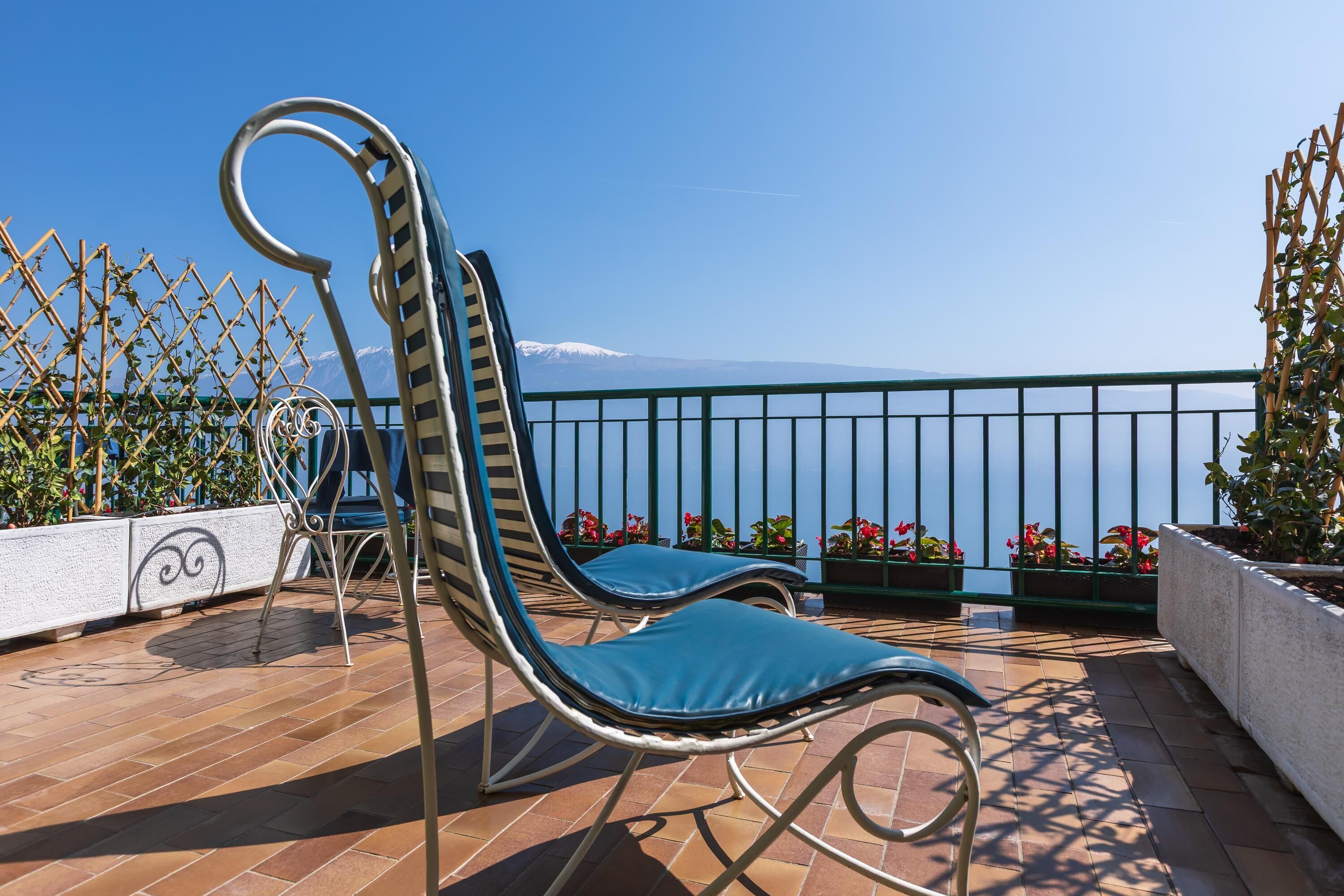 A terrace with two lounge chairs, a metal railing, and a view of the sea.