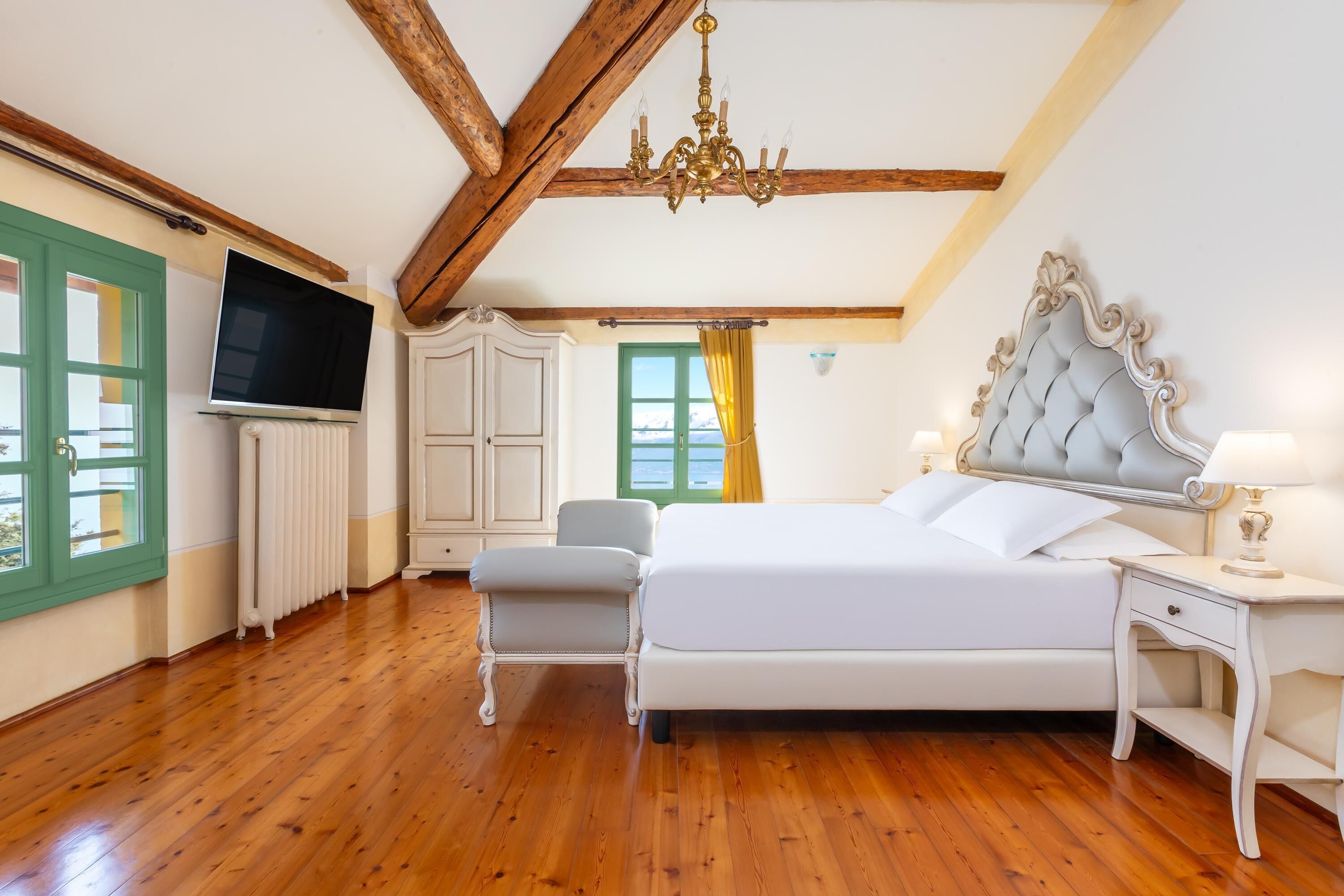 A bedroom with a large bed, a TV, a chair, and a window with curtains.