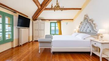 A bedroom with a large bed, a TV, a chair, and a window with curtains.