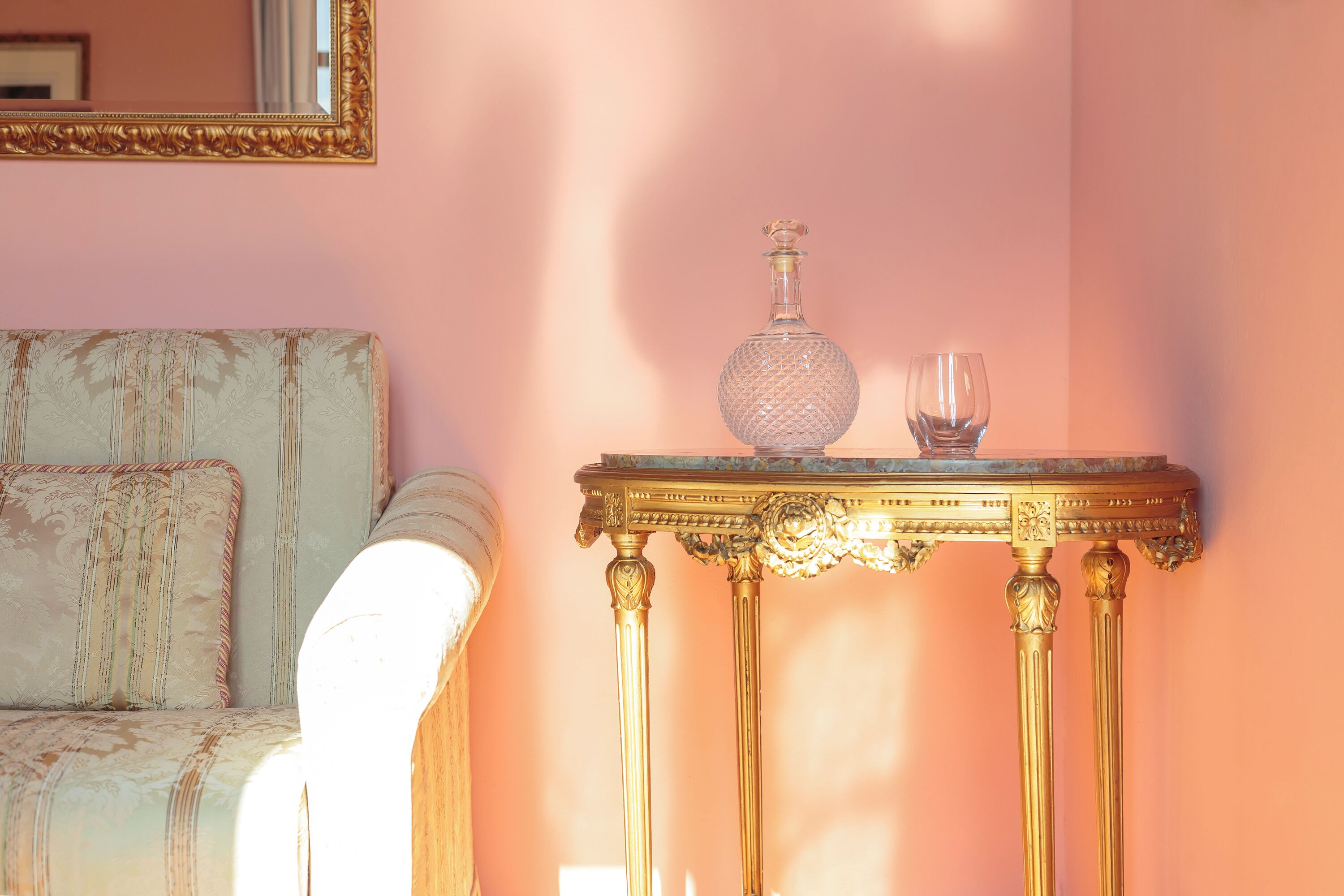 A room with a vintage sofa, a gold ornate table, and a decorative glass bottle.