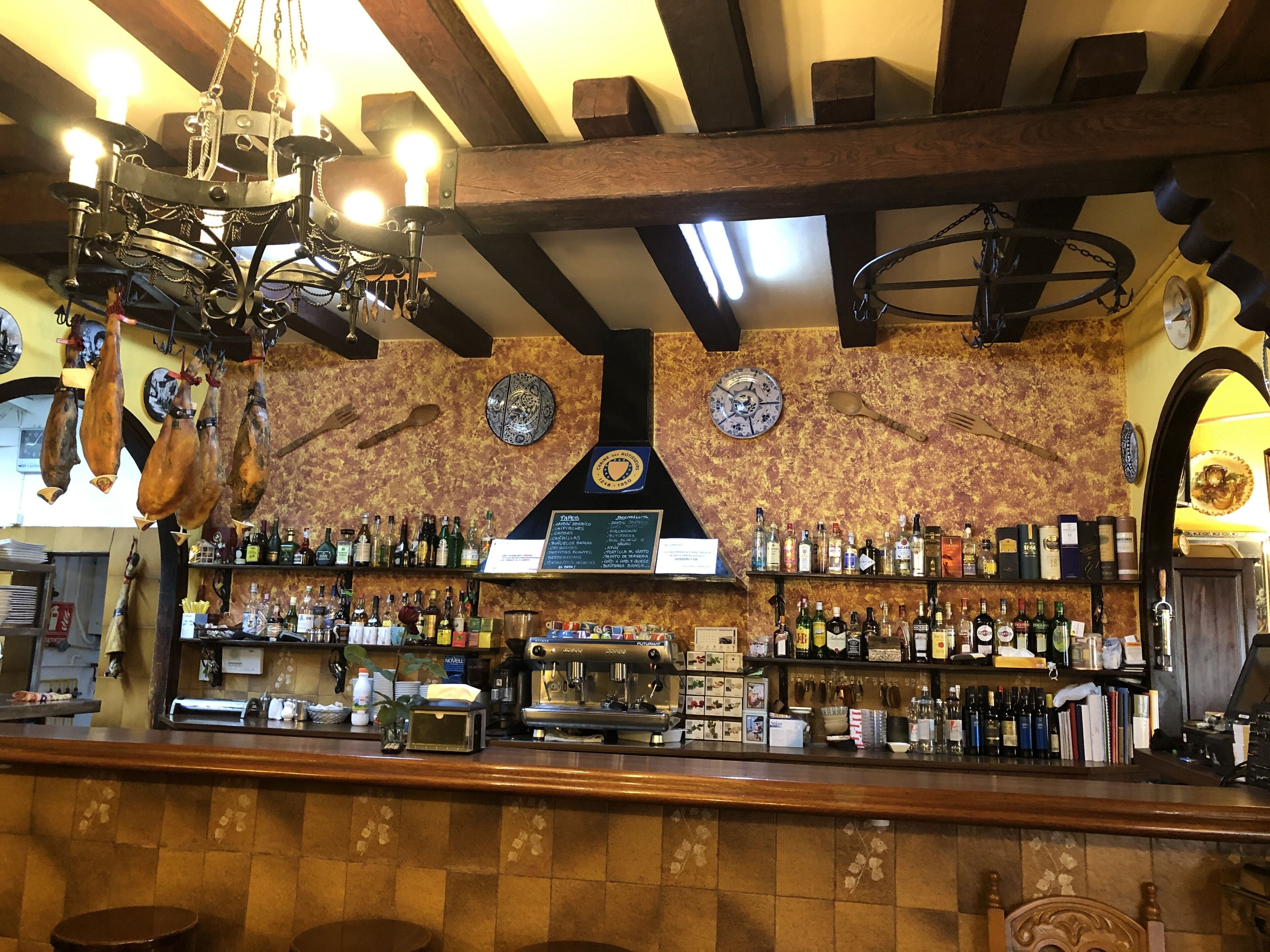 Un bar con mostrador de madera, estantes llenos de botellas de licor, una máquina de caf é y carne colgando.