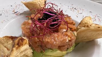Un plato con corteza dorada, capas verdes y cobertura de ingredientes rosa y negros, servido sobre un plato blanco con especias dispersas.