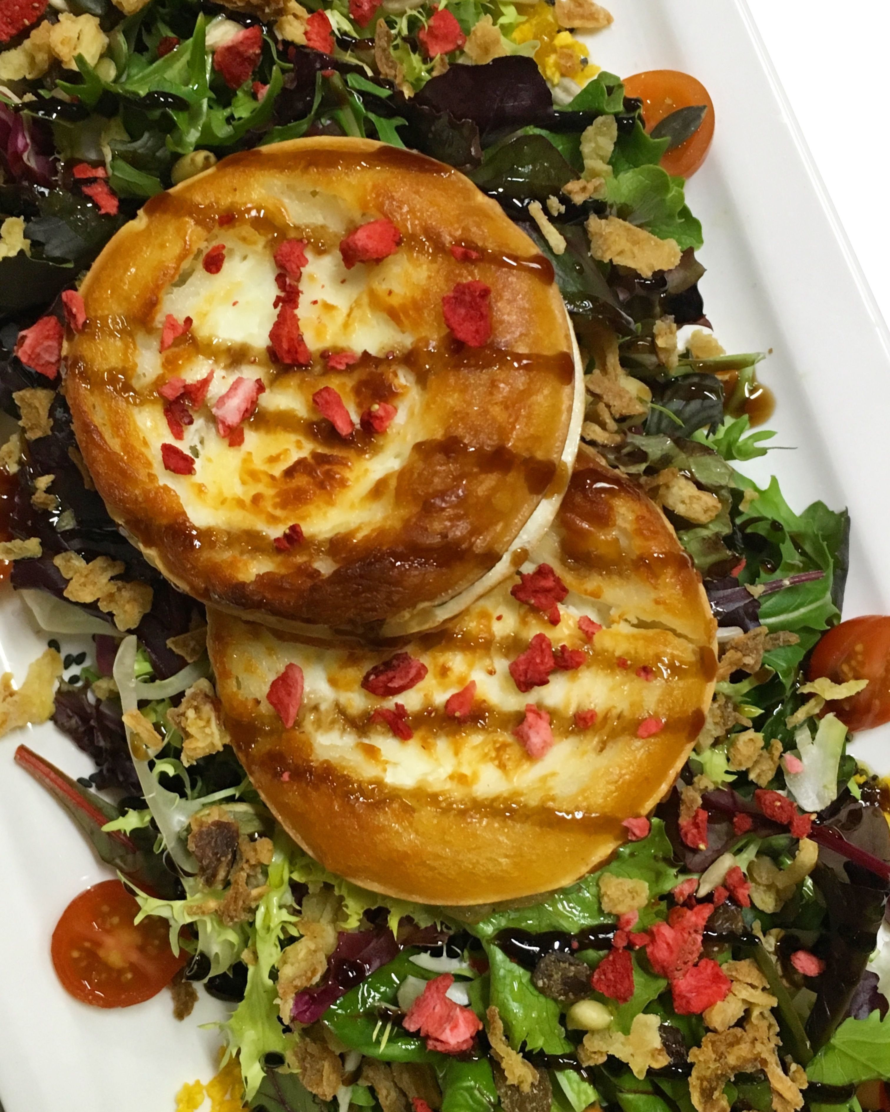 Un plato con dos sándwiches abiertos cubiertos de queso y hojuelas de chile rojo, rodeado de una ensalada mixta con croutons y tomates cereza.