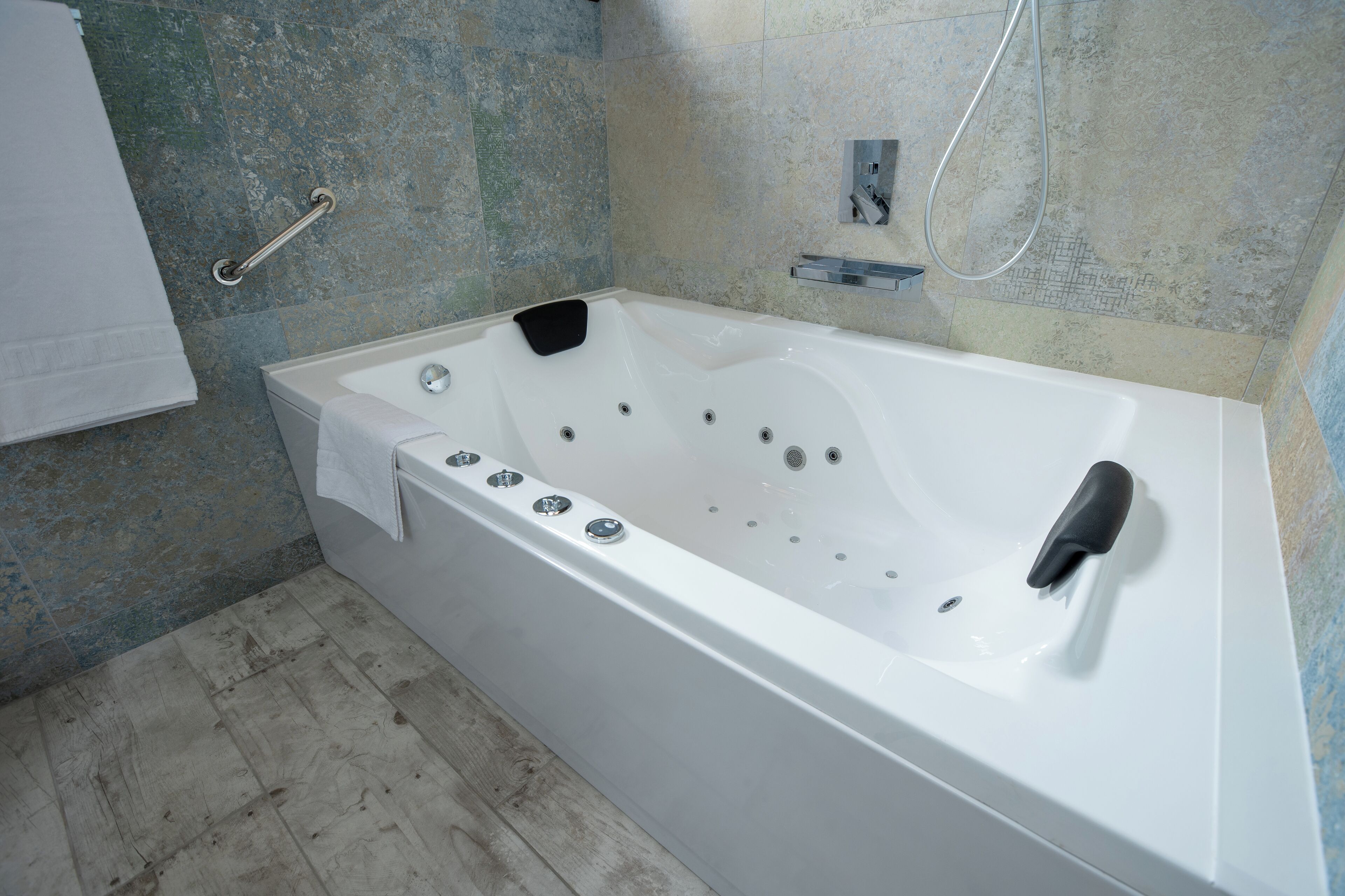 A modern bathroom with a white bathtub, a handheld showerhead, and a grab bar.