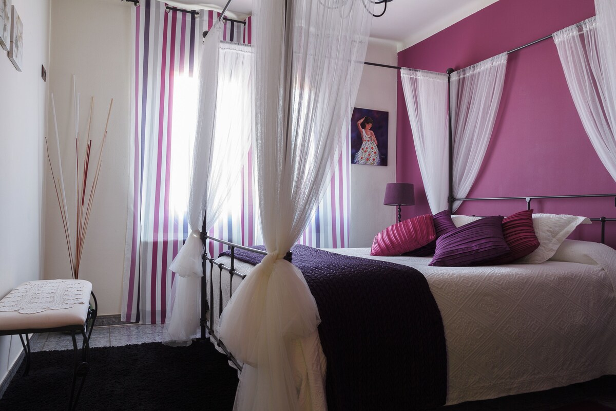 Un dormitorio con cama, un banco y una ventana con cortinas.