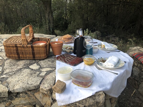 An outdoor dining setup with a white tablecloth, wicker basket, candles, food items, and a water bottle.
