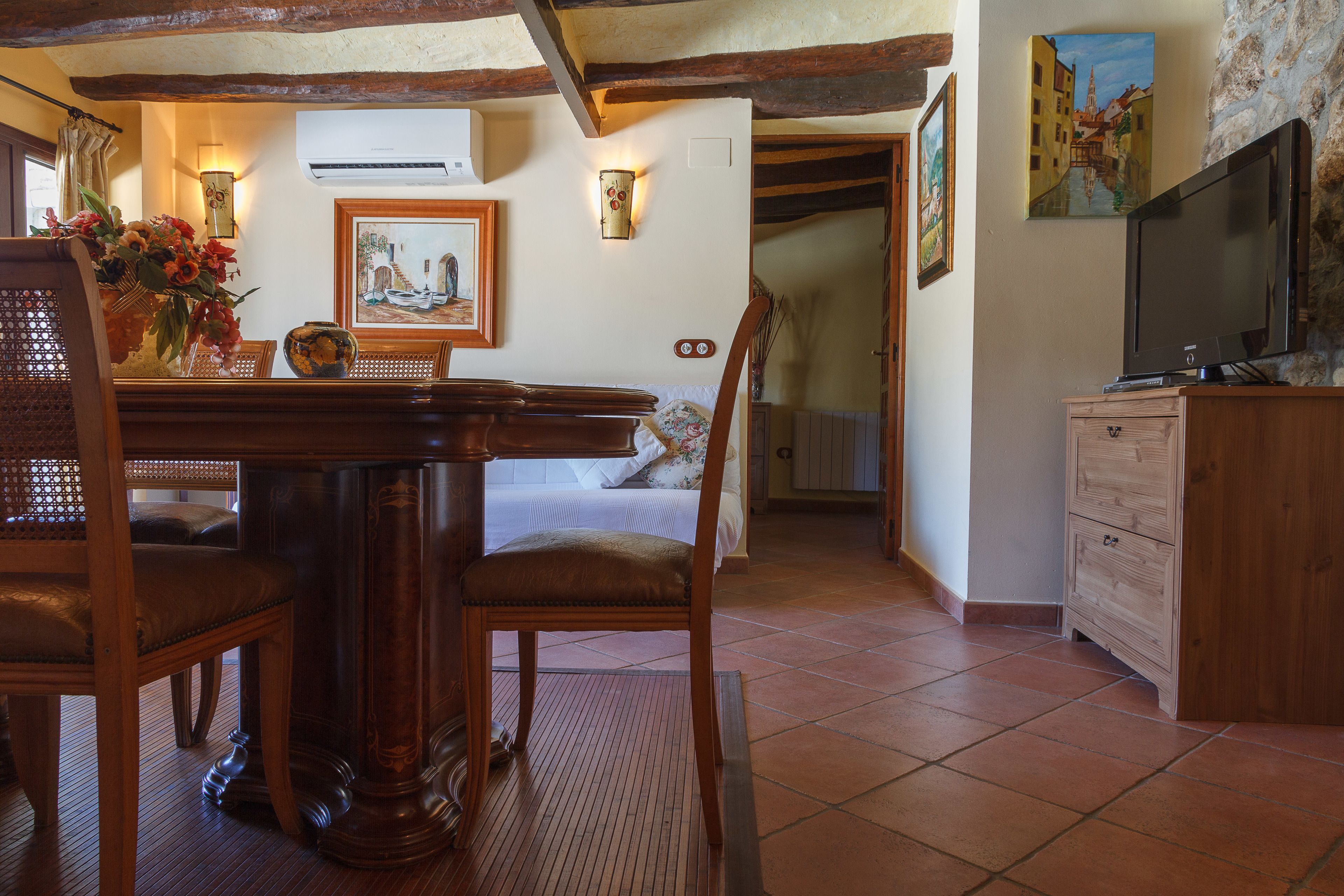 Una habitación acogedora con una mesa de comedor de madera, sillas, una cama y un televisor sobre un mueble de madera.