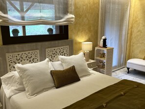 A neatly made bed with white and brown pillows, a green throw, and a nightstand with a lamp and decorative items.